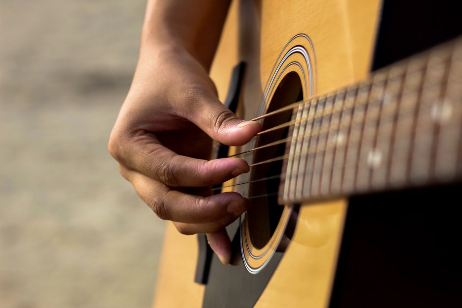 Detailed view of a hand strumming an acoustic guitar outdoors, capturing musical passion.