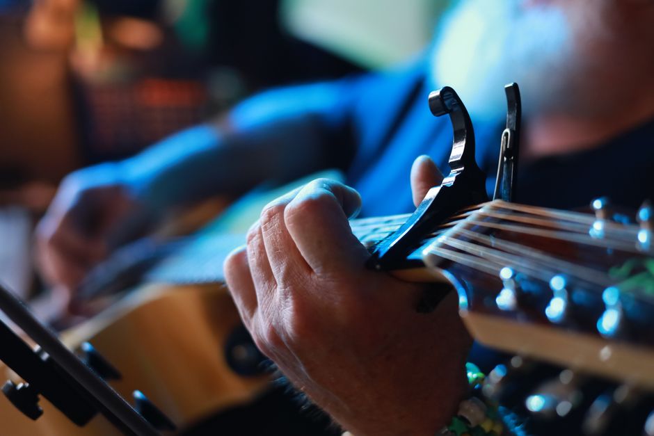 Detailed view of hands playing guitar with capo, capturing musician's skill and emotion.