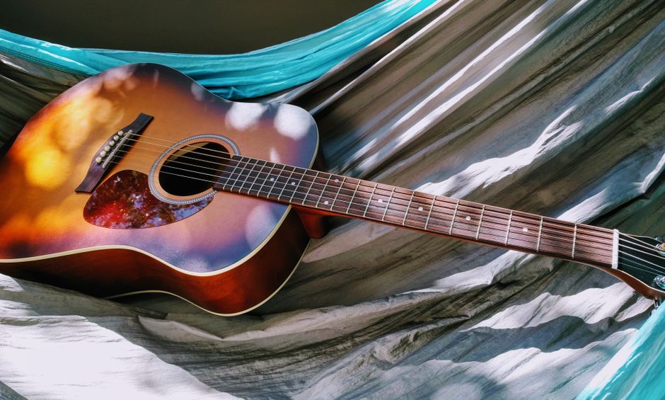 Sunburst dreadnought acoustic guitar resting on a hammock in dappled light