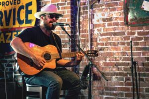 Solo musician playing an acoustic guitar and singing on a stool in a bar